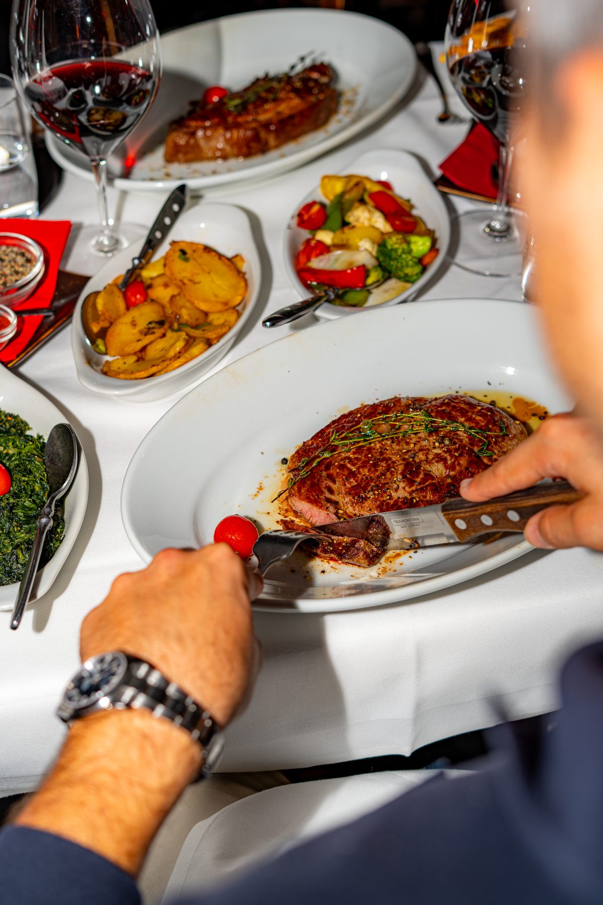 Gast schneidet ein Steak mit Bratkartoffeln, Gemüse und Rotwein